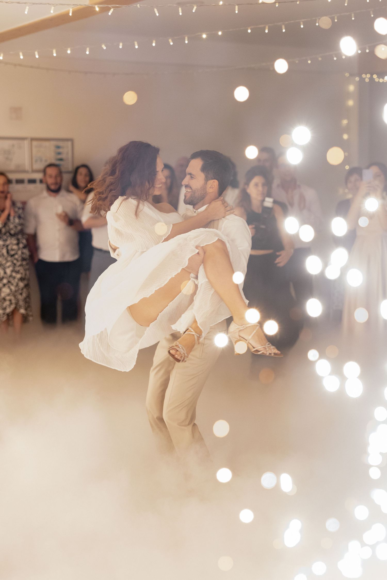 A couple performs their first dance at their wedding reception under twinkling string lights.