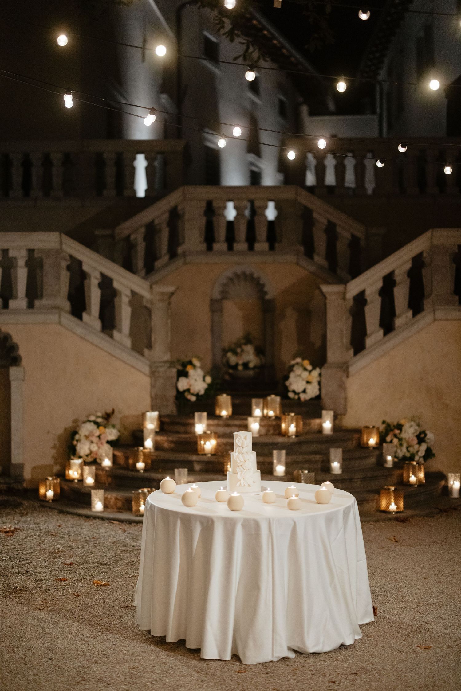 Elegant white round tables with candles set up for wedding reception under string lights.