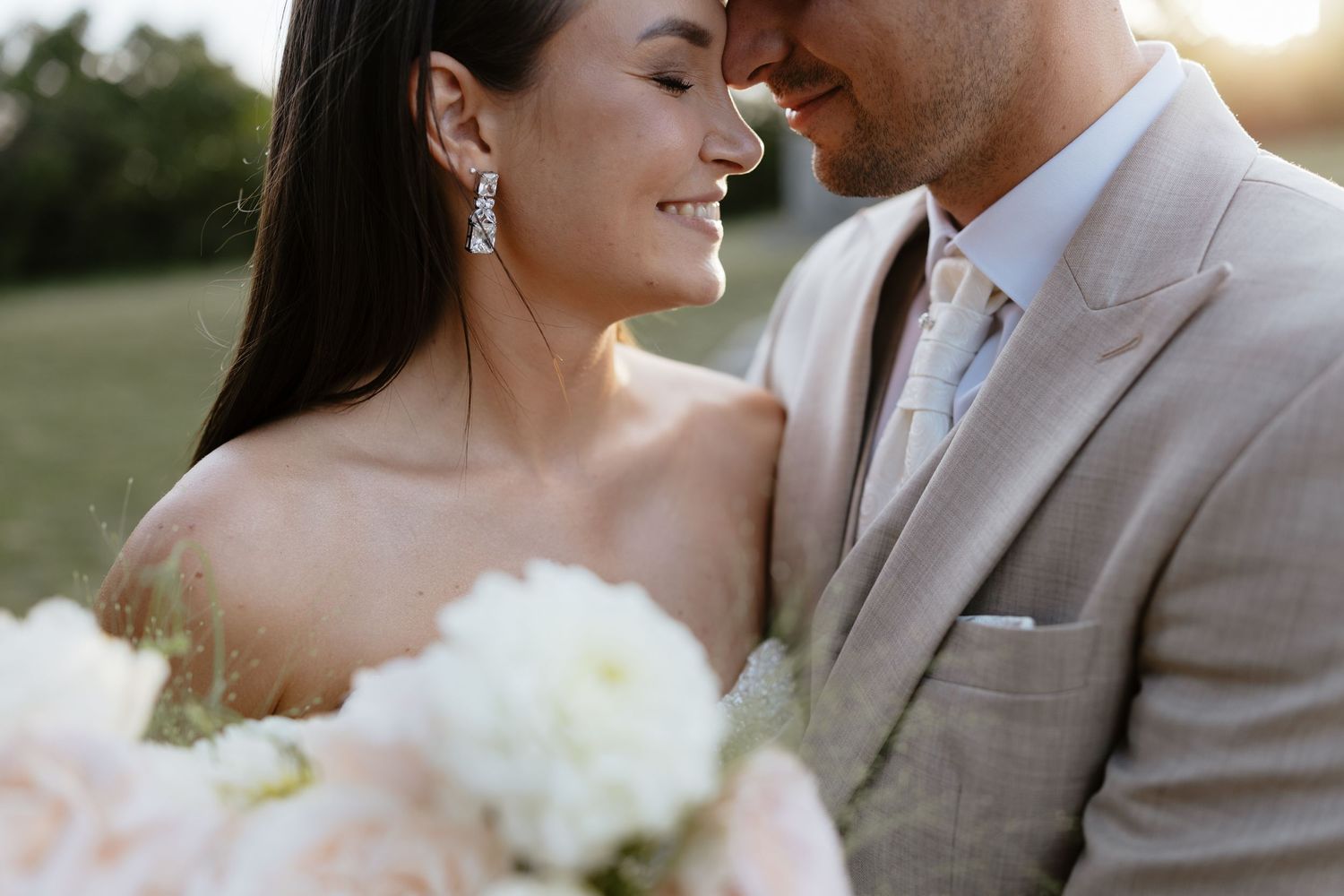 Romantic wedding couple shares an intimate moment at sunset with soft lighting and delicate floral bouquet.