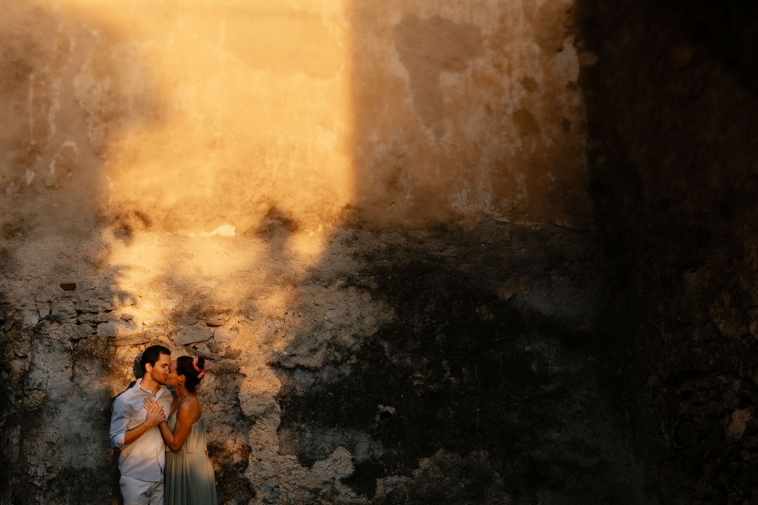 Couple silhouetted against weathered stone wall in warm sunset light.