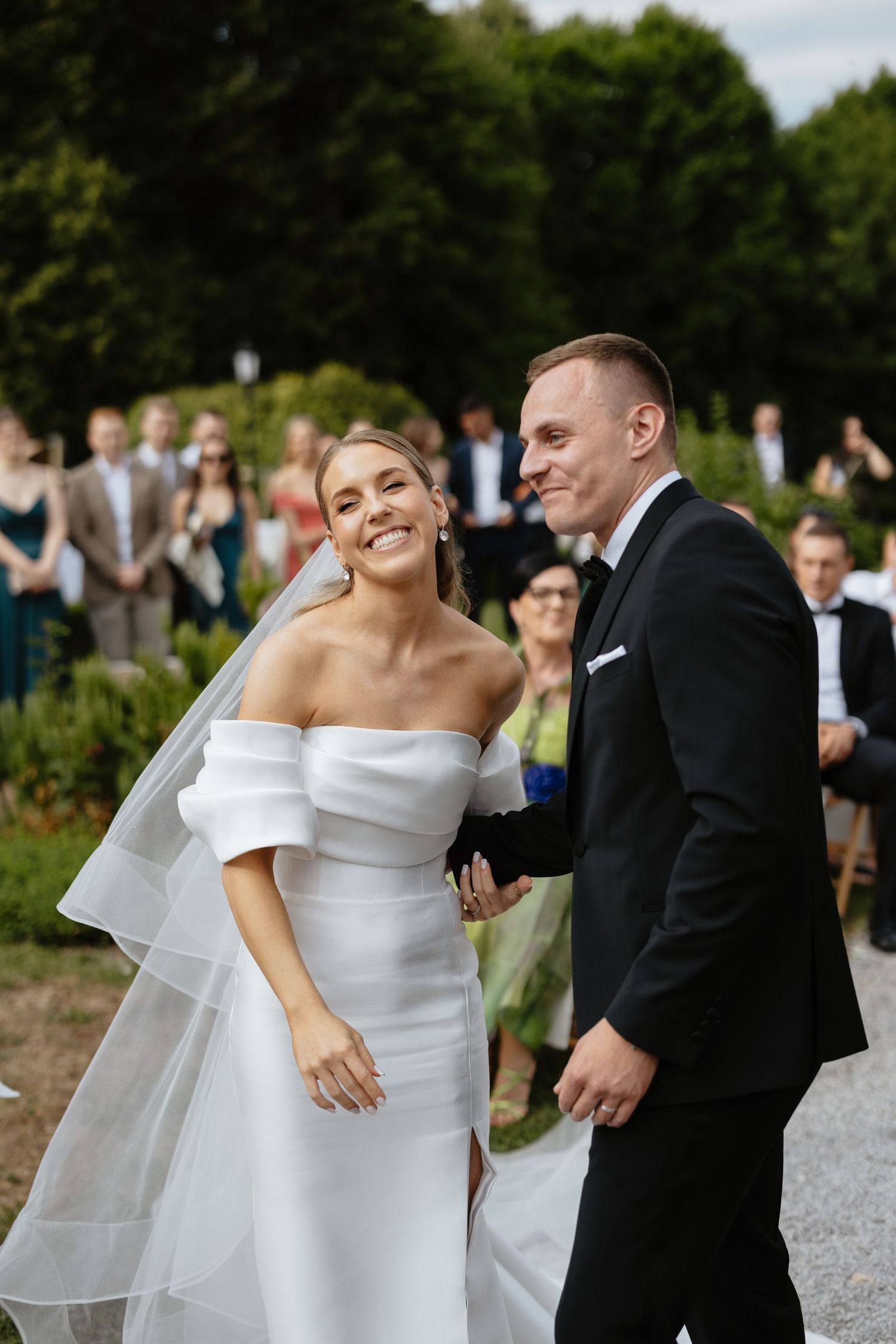 Joyful outdoor wedding moment with guests in background.