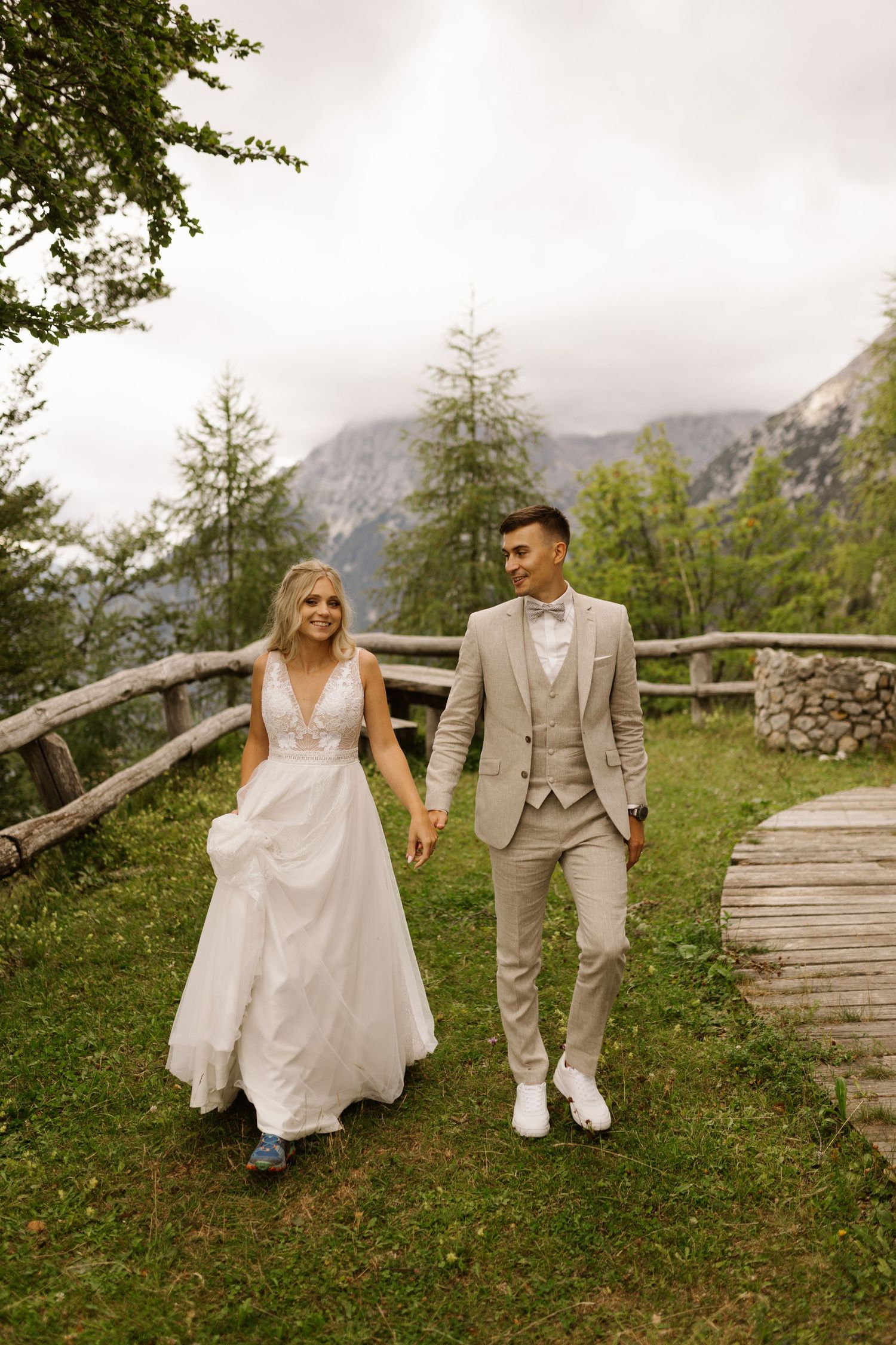 A couple sits together on rustic wooden benches surrounded by alpine meadow and mountain scenery.