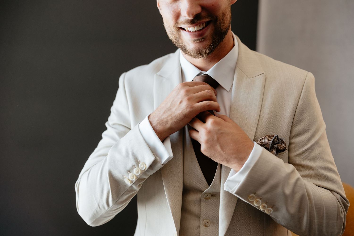 A person adjusts their tie while wearing a crisp white suit jacket with a patterned pocket square.