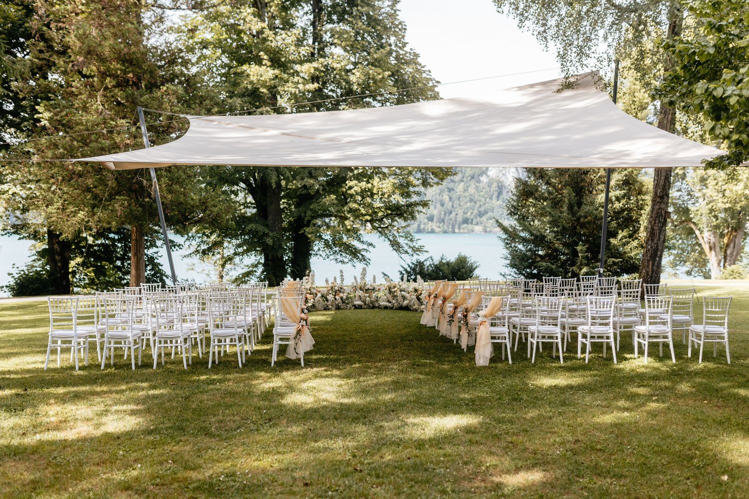 Outdoor wedding ceremony setup with white chairs and canopy in a serene garden setting.