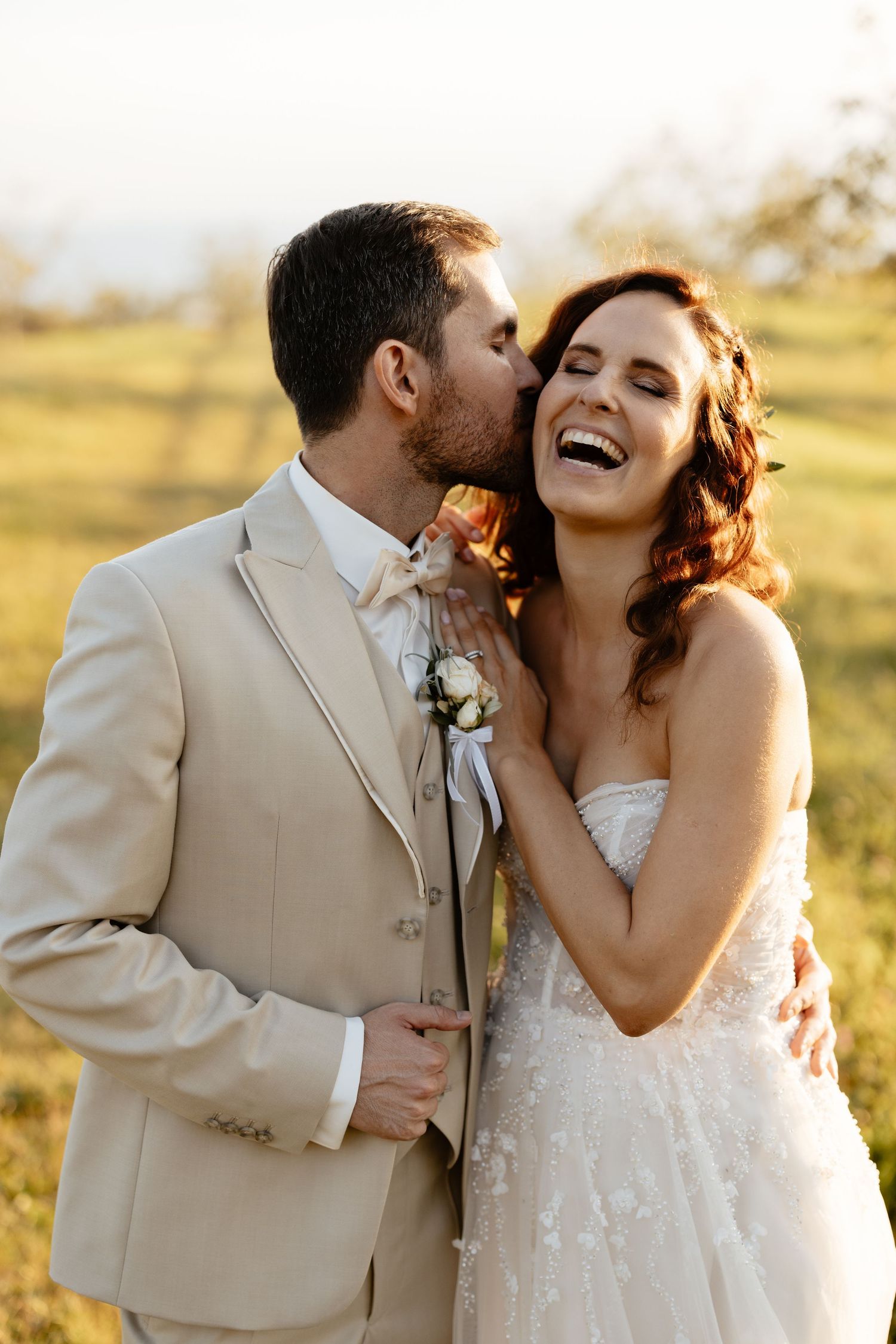 Romantic sunset wedding portraits of a couple laughing and embracing in a golden field.