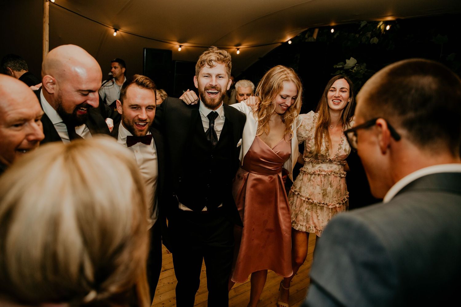 Wedding reception guests dance and celebrate under warm lighting in an intimate indoor venue.