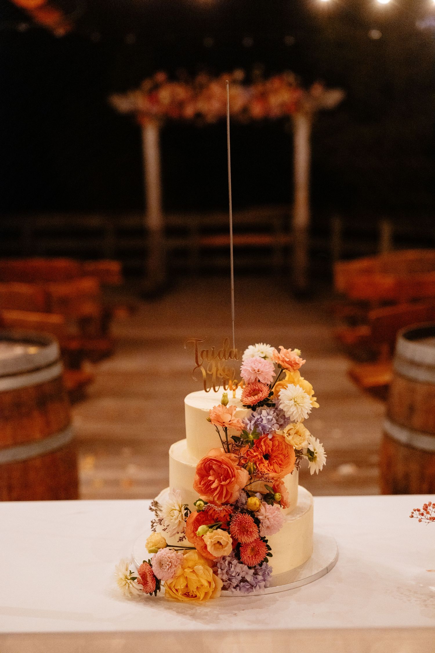 Elegant three-tier wedding cake decorated with cascading autumn-colored fresh flowers on a rustic display.