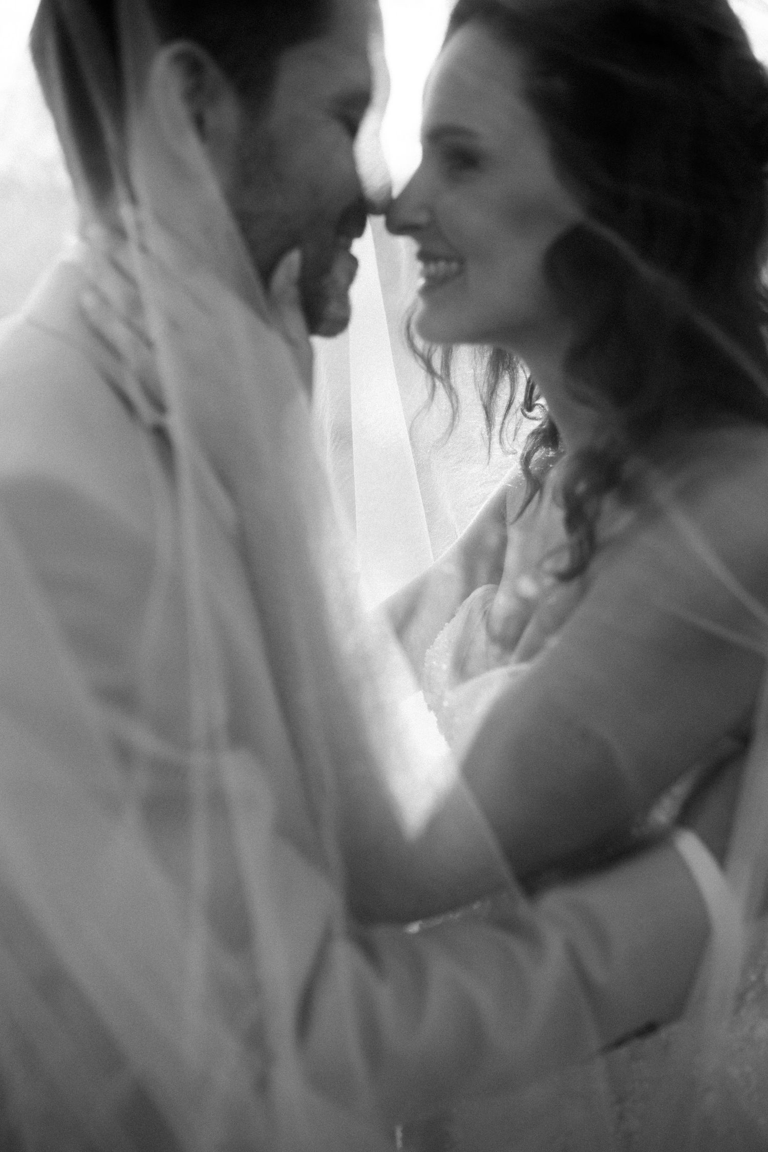 An intimate black and white portrait of newlyweds sharing a tender moment under a veil.