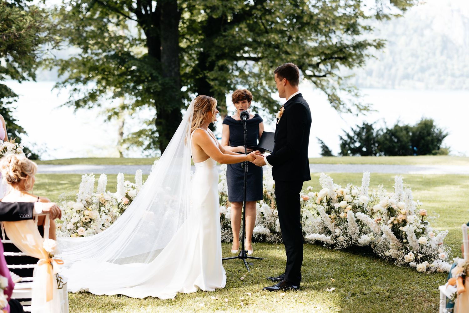 Outdoor wedding ceremony with floral decorations and guests gathered on a sunny day.