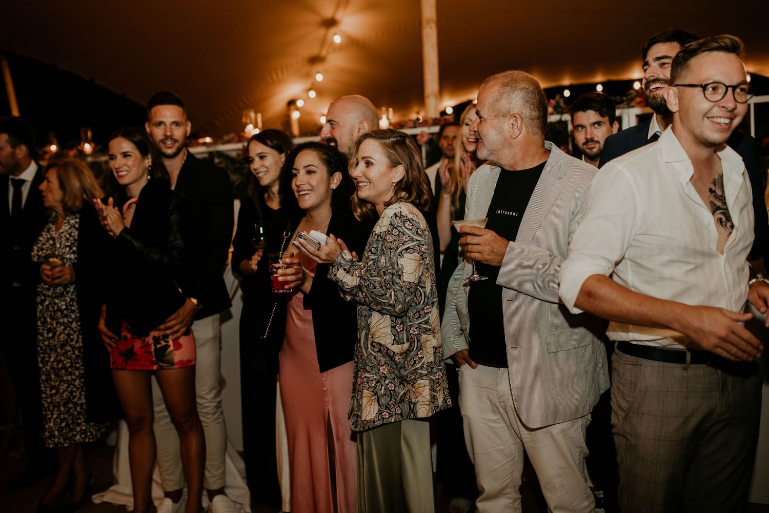 Wedding reception guests mingling and dancing in a dimly lit venue with warm ambient lighting.