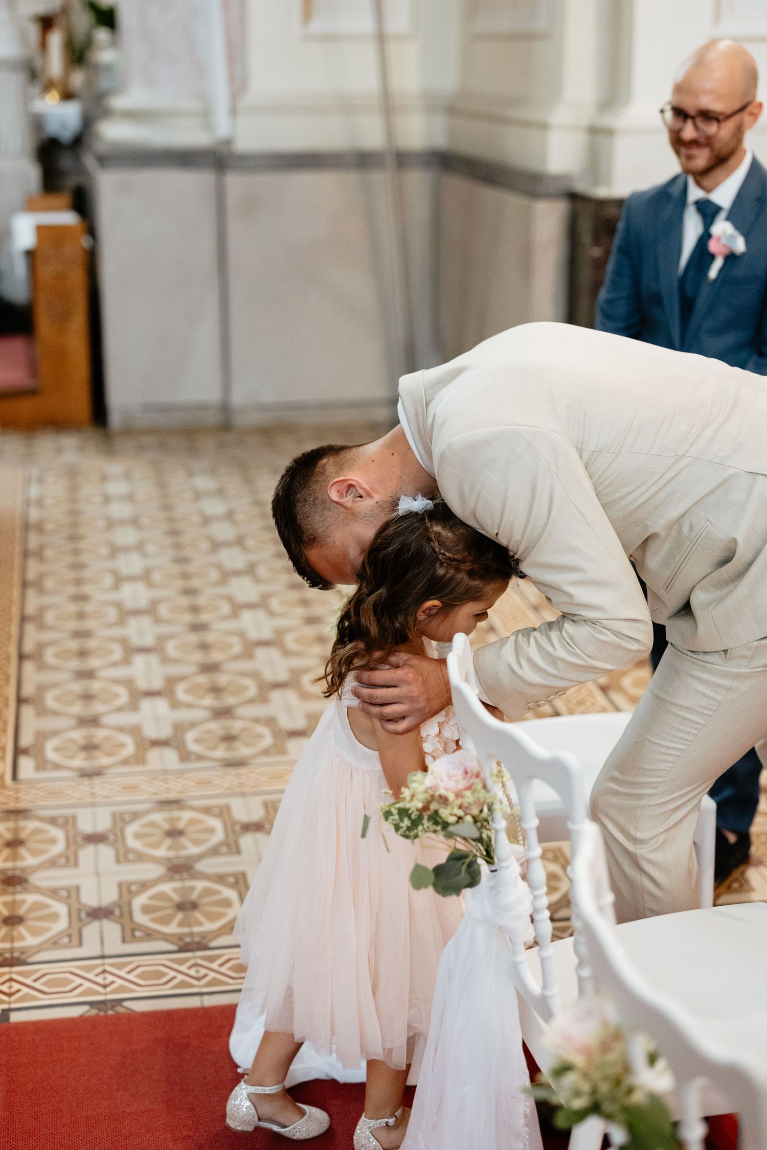 Sweet moment during wedding ceremony as couple interacts with young attendant in white dress.
