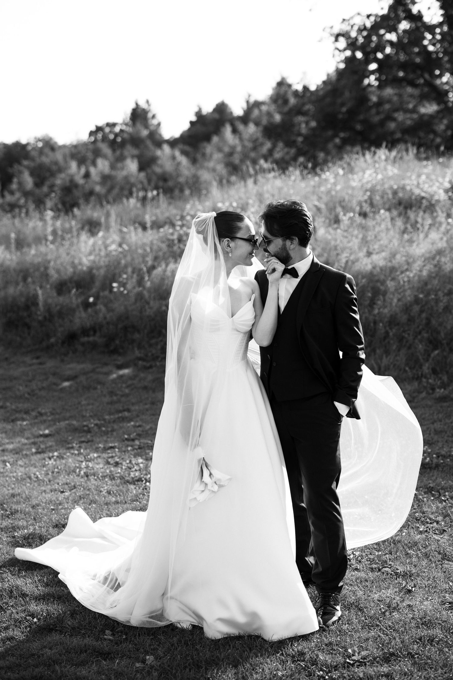 A black and white romantic wedding portrait captured in a windswept meadow.