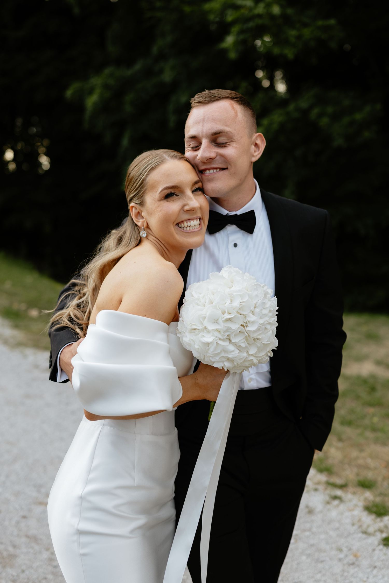 Wedding couple in elegant white dress and black tuxedo sharing intimate moments outdoors.