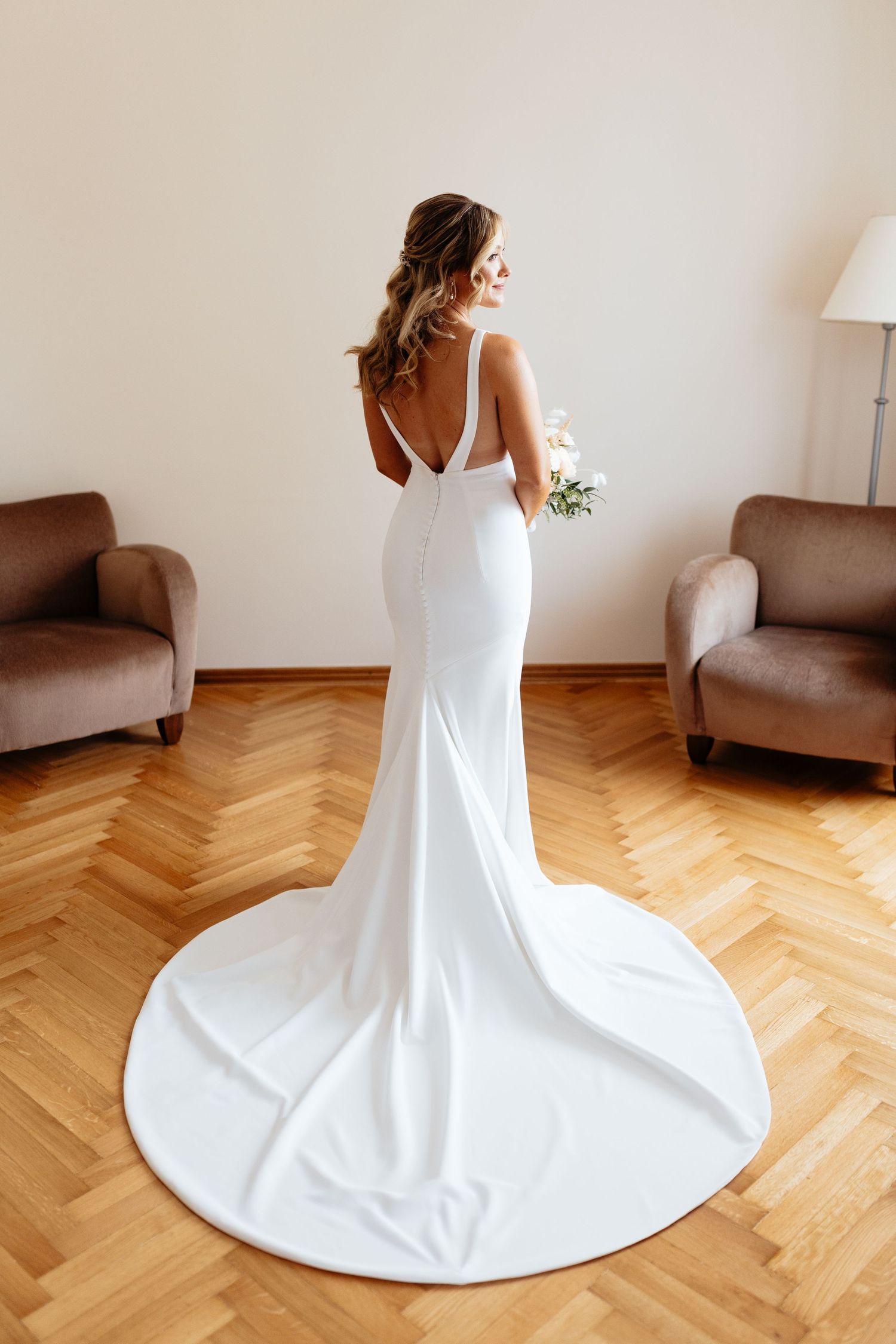 Elegant white wedding dress with a flowing train displayed on herringbone wood flooring.