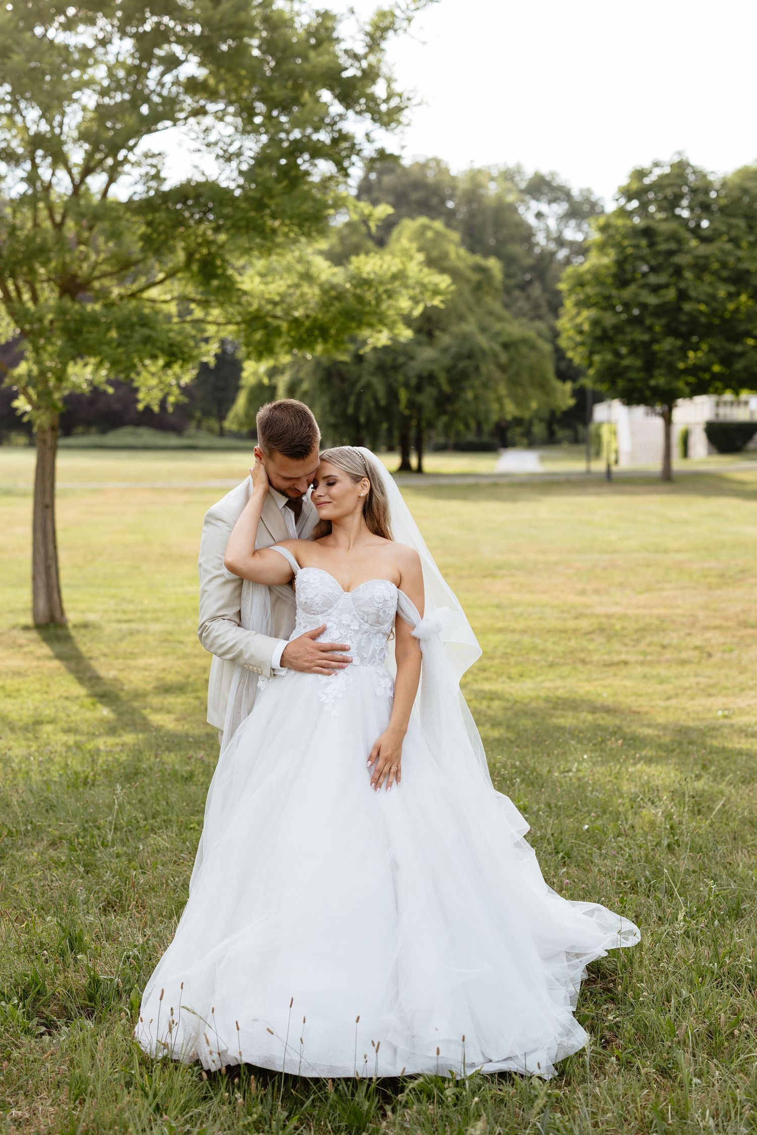 Newlyweds embrace in a sunlit garden setting during their wedding photoshoot.