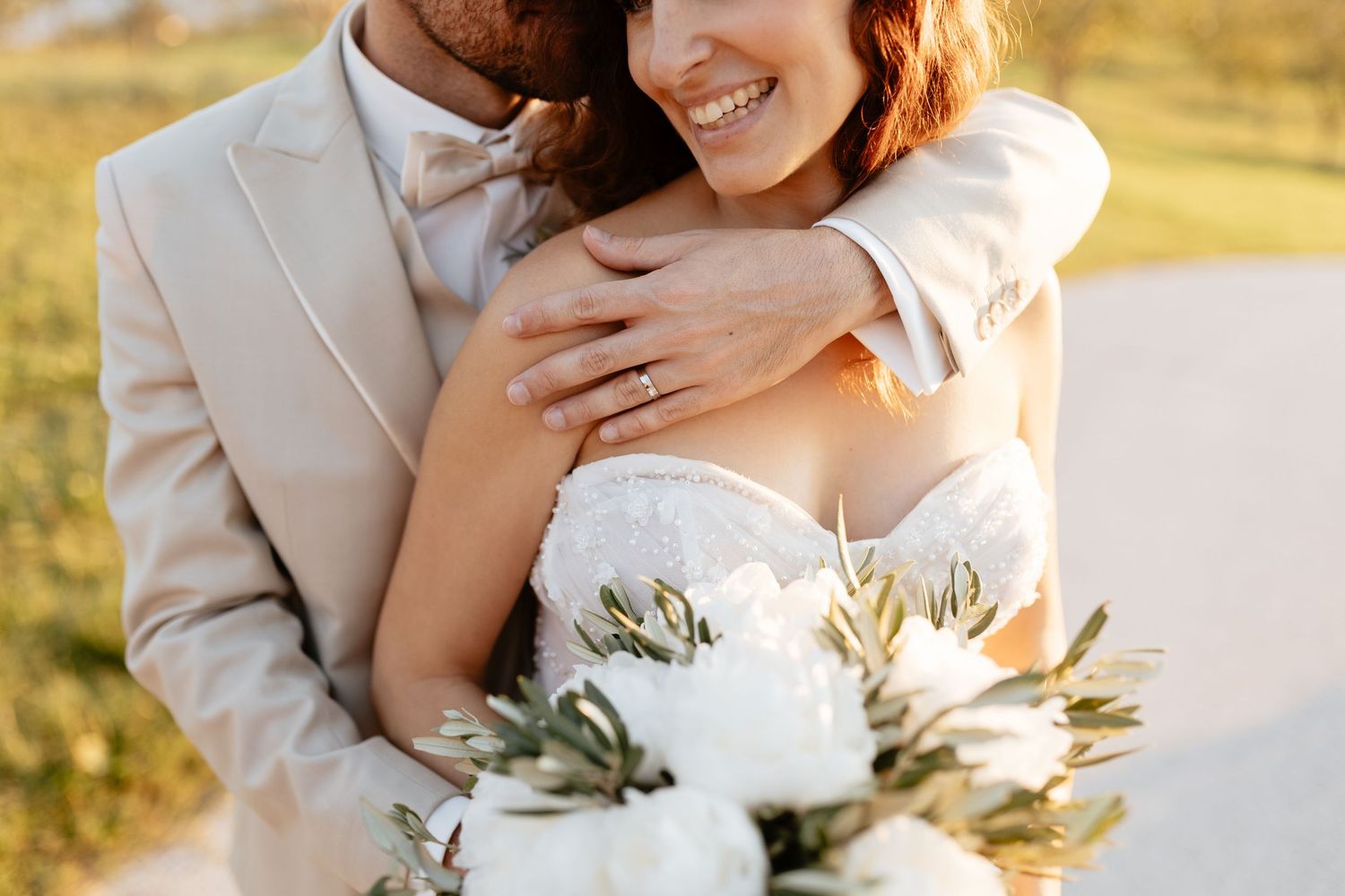 Intimate wedding moment captured in warm sunset light with white floral bouquet details.