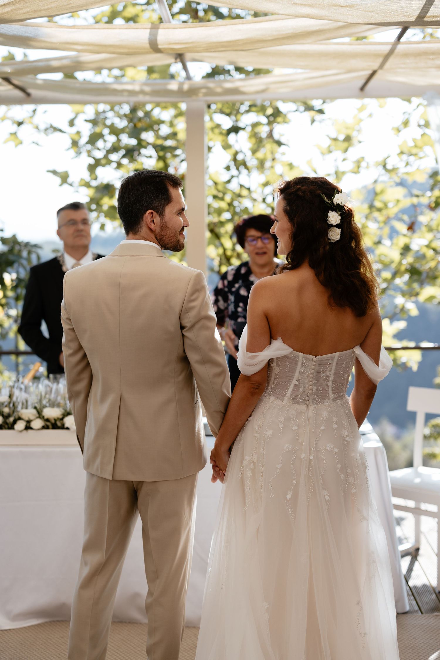 Wedding couple and guests walking together indoors under white canopy with natural lighting.