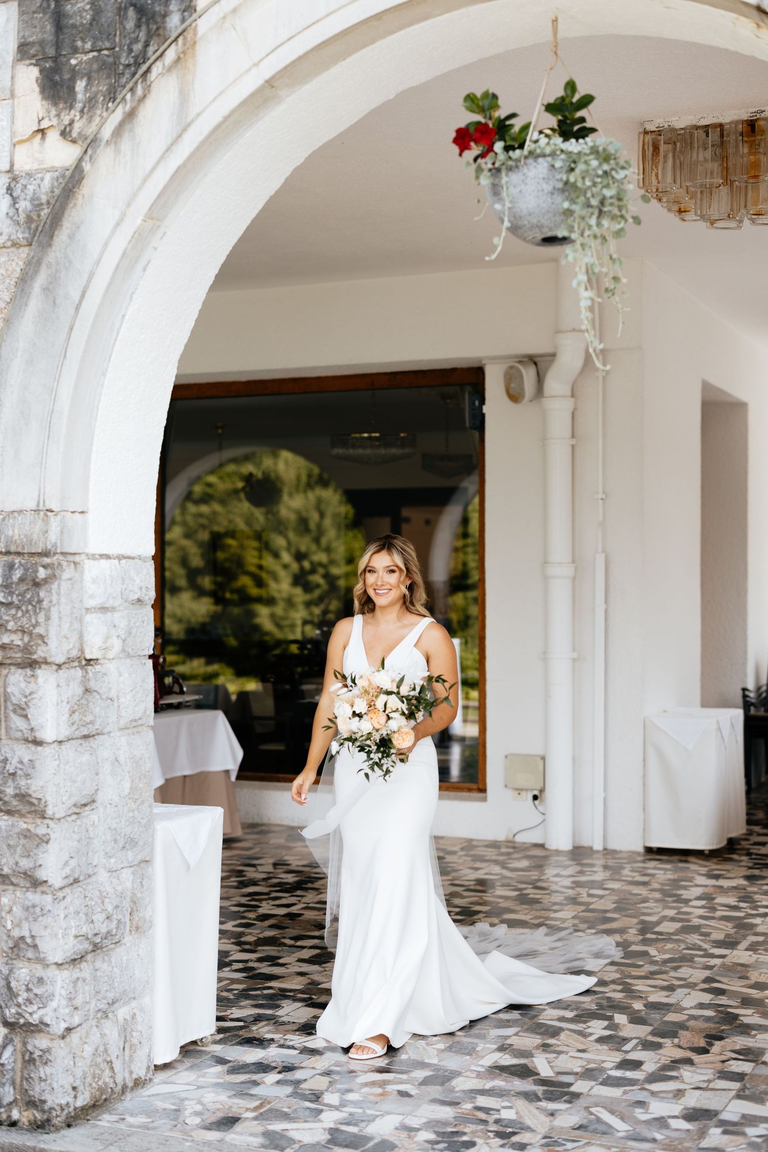 Bride in white dress poses under stone archways at an elegant venue.