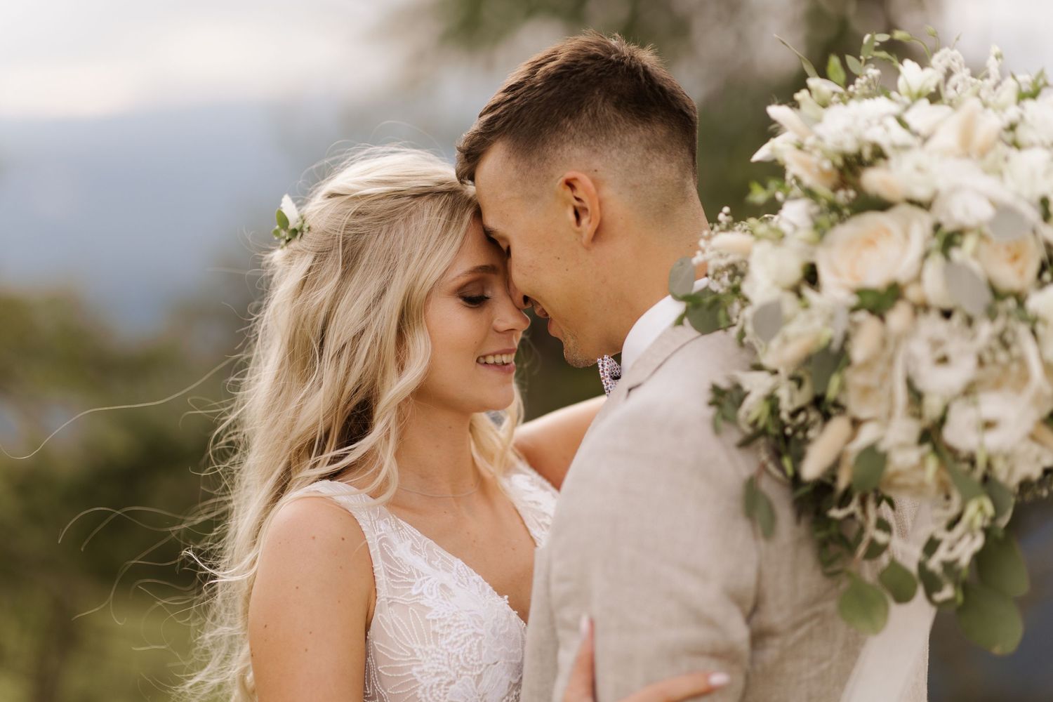 A couple shares romantic moments in a series of elegant outdoor wedding photos with white floral arrangements.