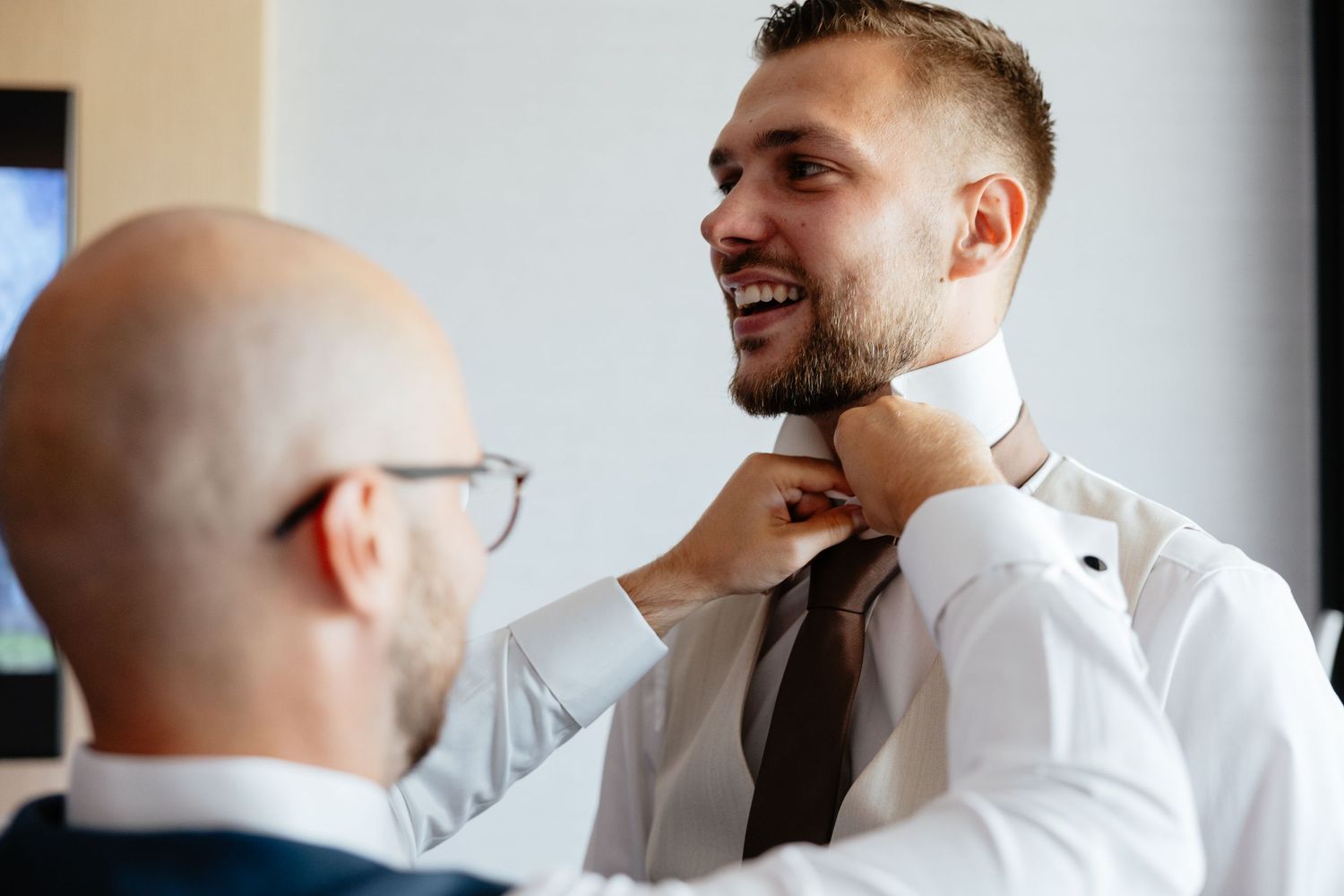 A man helps adjust another person's tie and collar while getting ready for formal occasion.