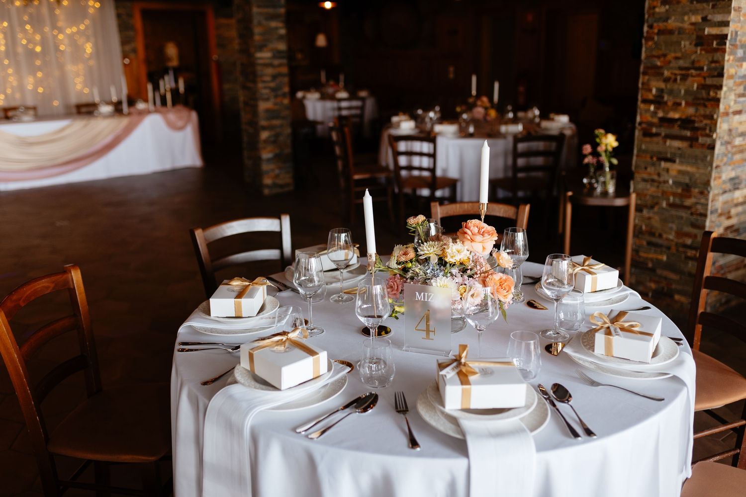 Elegant wedding reception tables set with white linens and centerpieces in rustic venue.