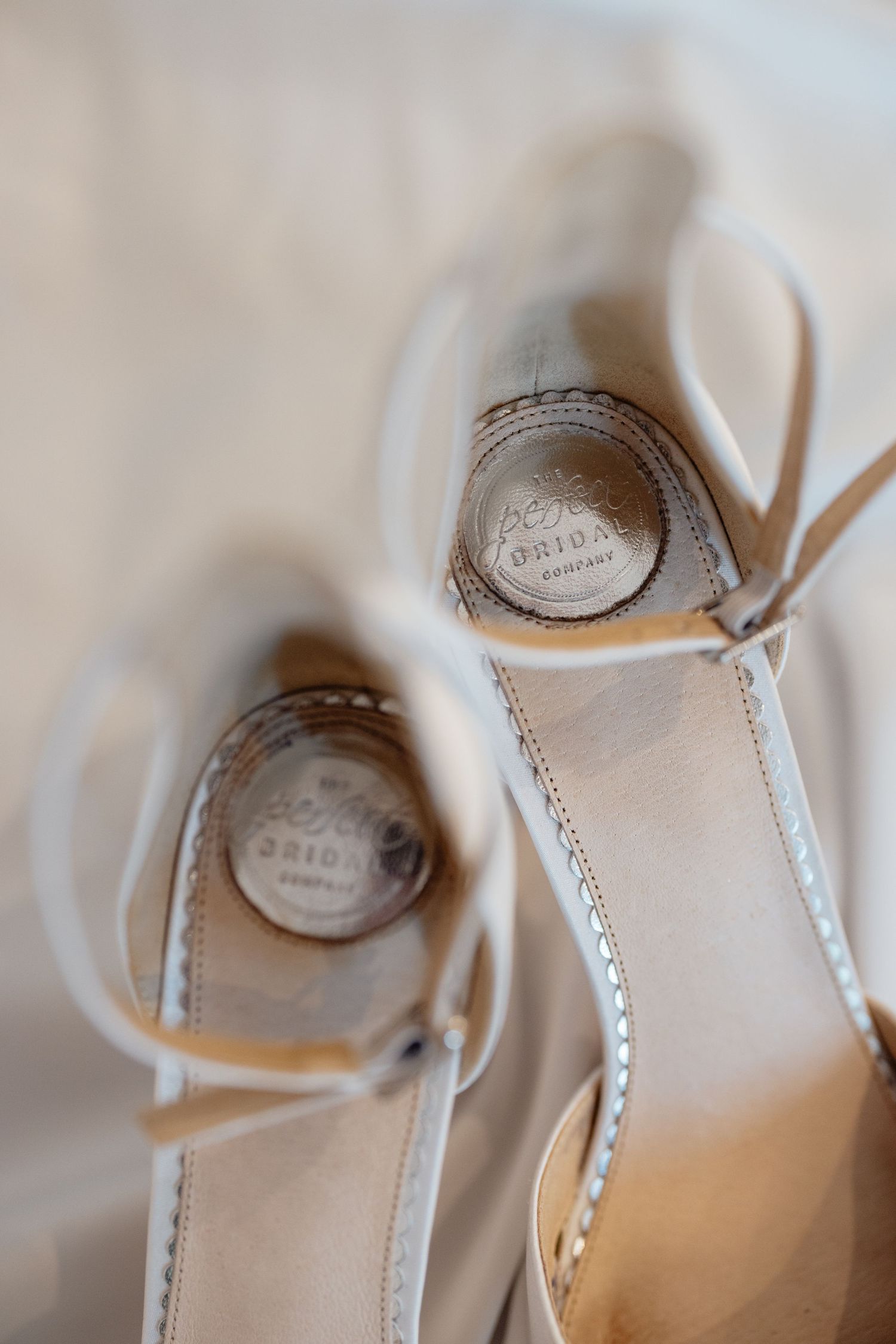 Close-up details of elegant white bridal shoes with delicate straps and embellishments.