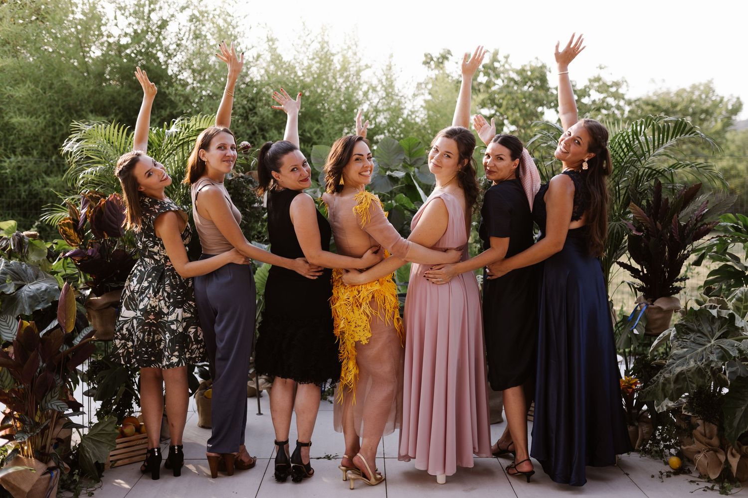 Wedding party lined up outdoors wearing mix of dark and light colored dresses.