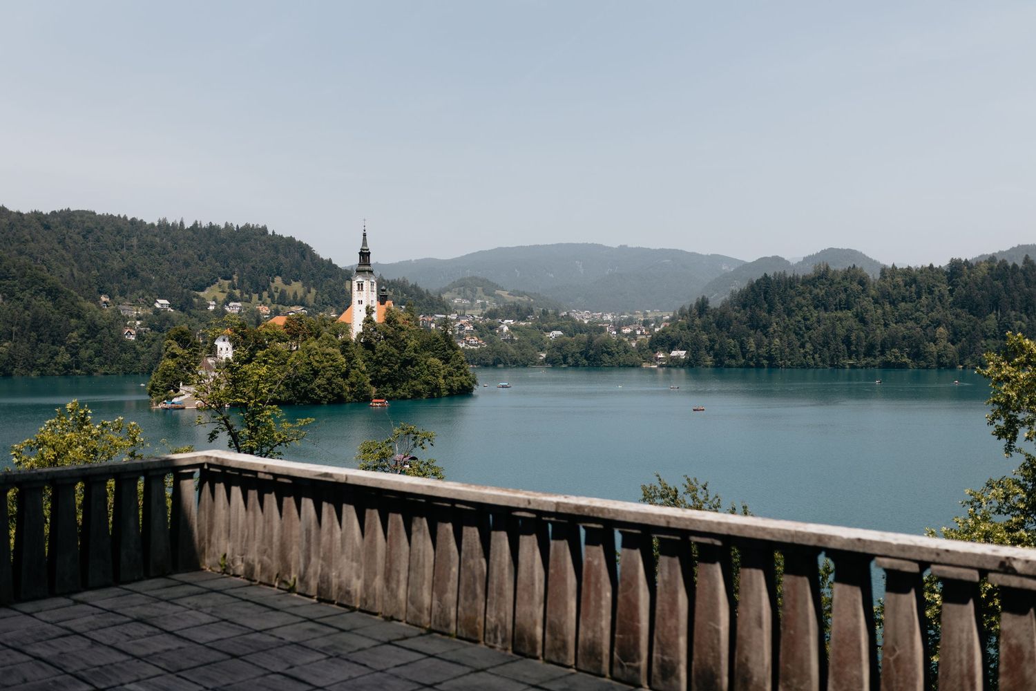 Scenic view of Lake Bled with church on island and wooden deck overlook framing the tranquil mountain landscape.