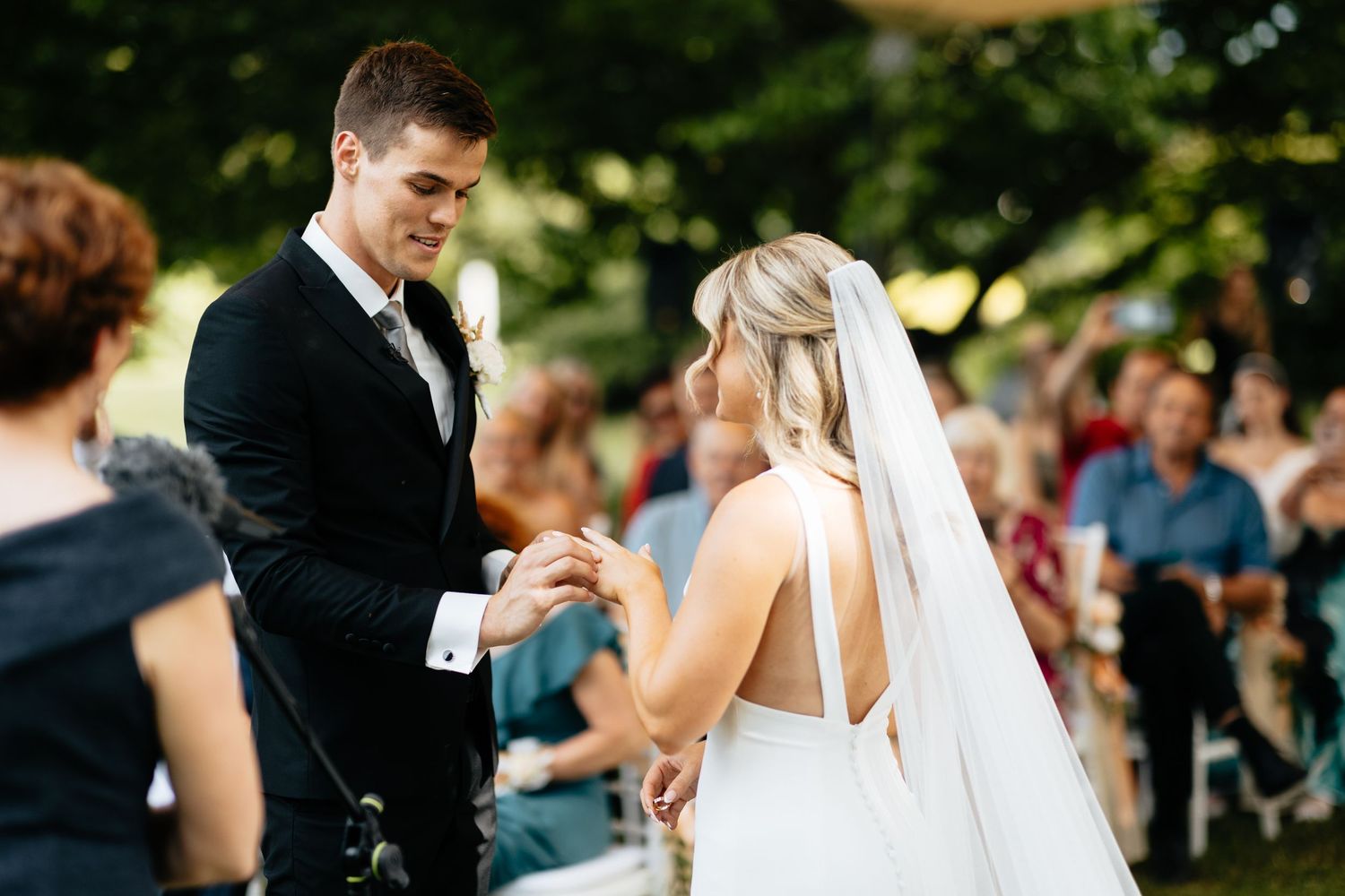 Wedding ceremony in a garden setting with guests watching the exchange of rings.