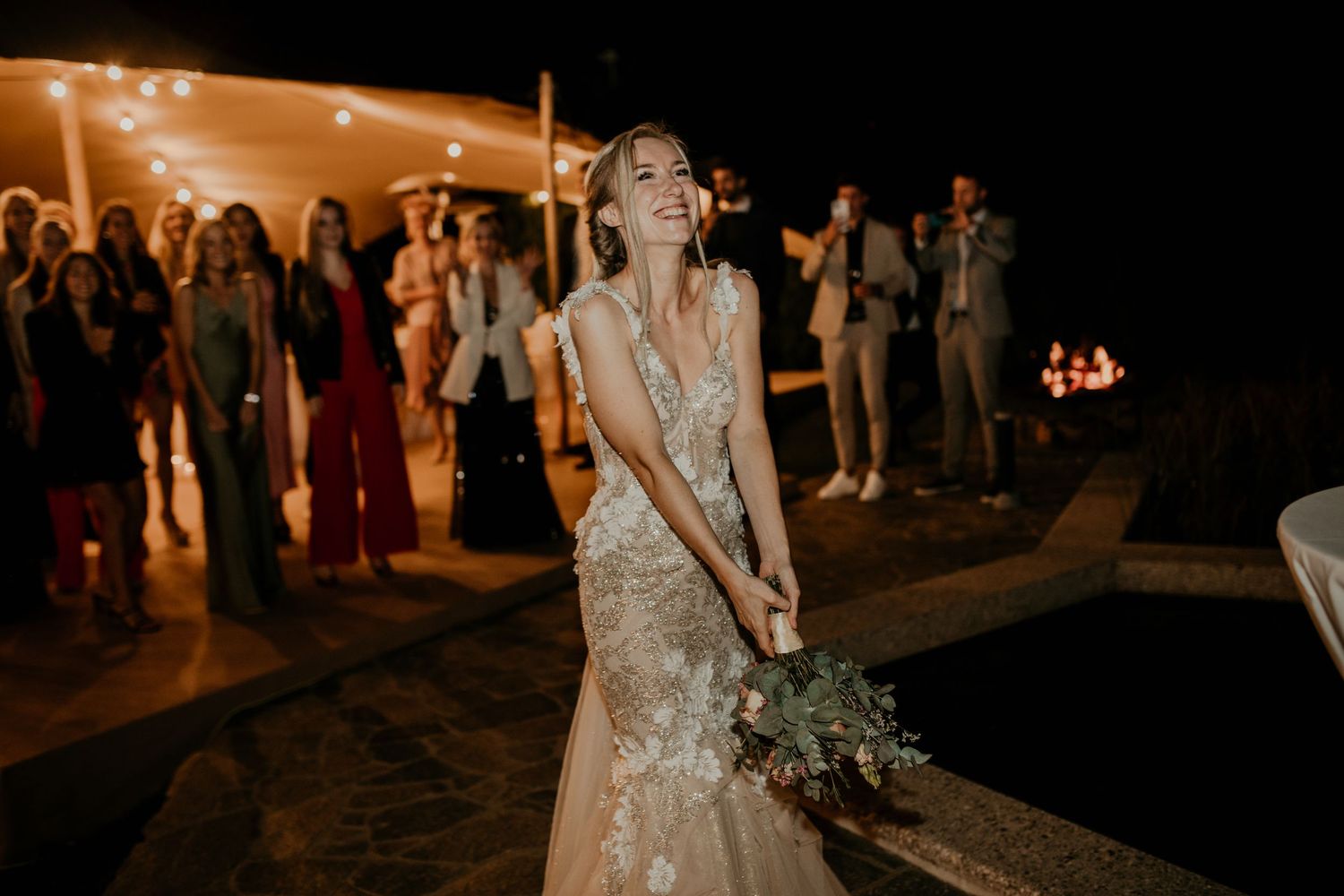 Wedding celebration at night with warm lighting and guests dancing in the background.