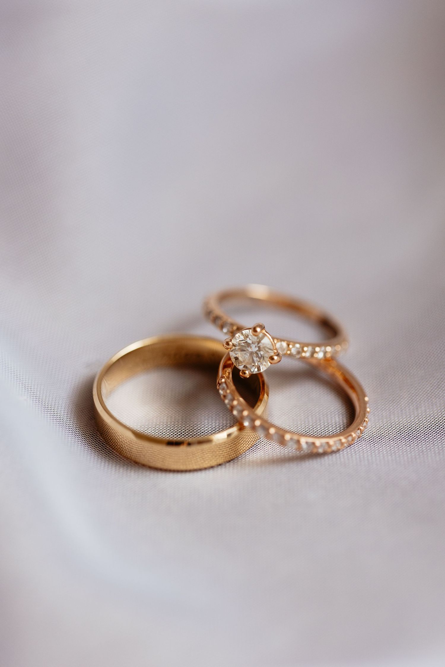 Close-up view of elegant gold wedding rings with diamonds on white fabric showing fine craftsmanship and detail.