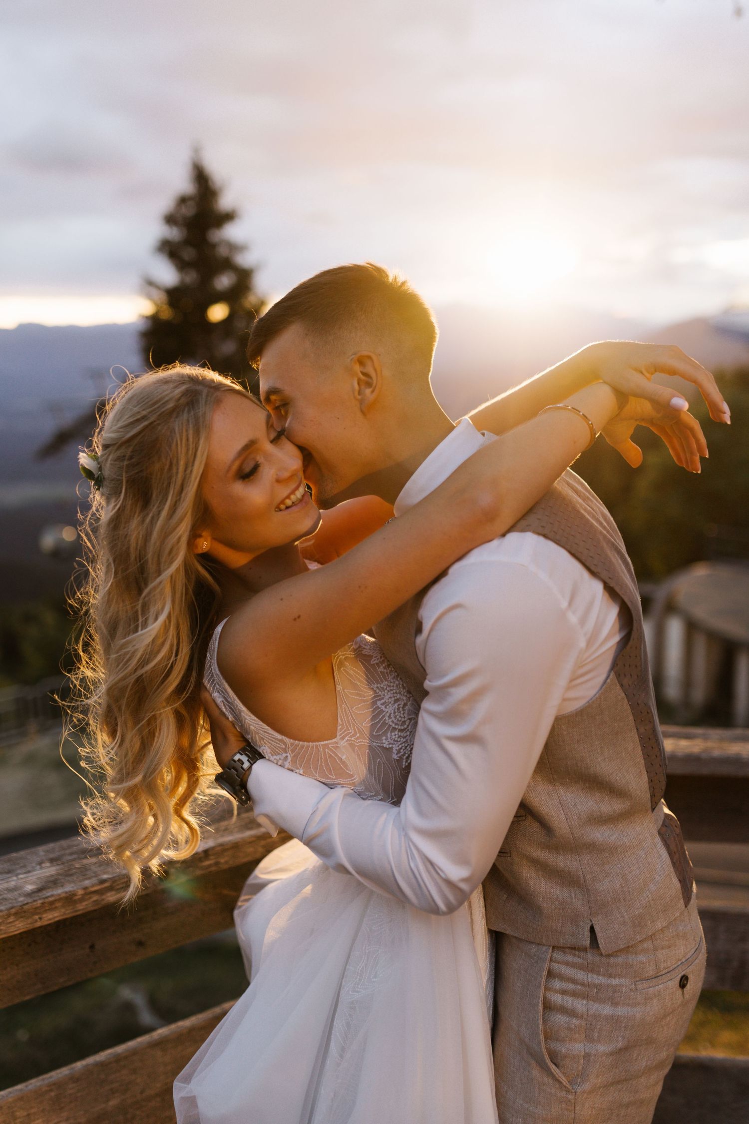 Romantic sunset wedding photo of couple in white dress and beige suit embracing outdoors.