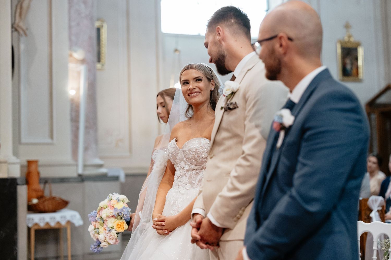 Wedding ceremony taking place in an elegant white church interior with ornate architectural details.