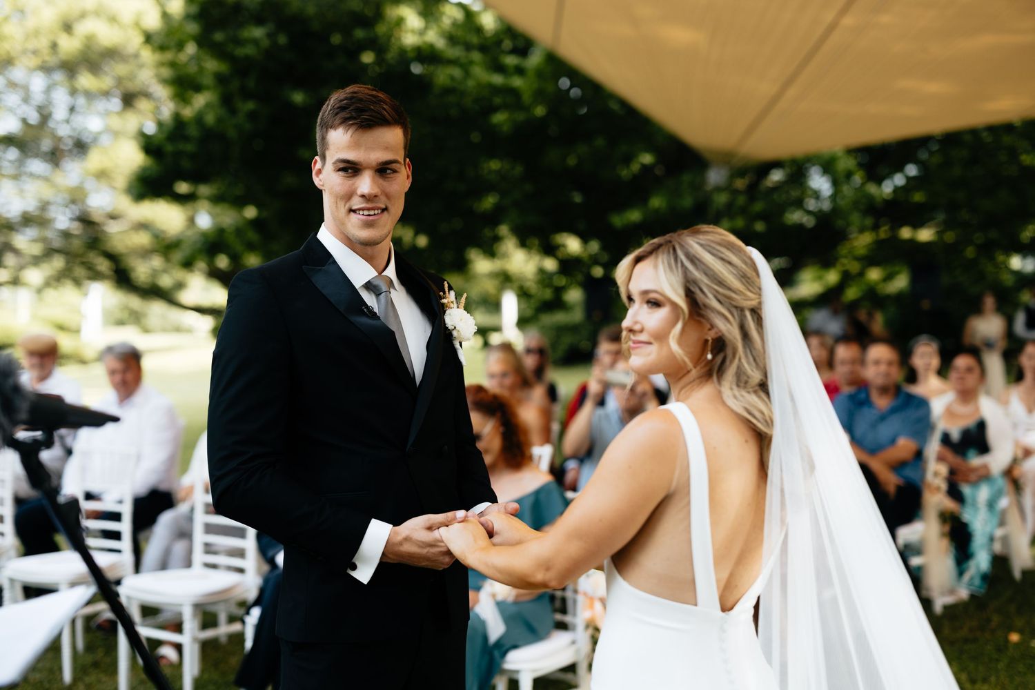Outdoor wedding ceremony under white umbrellas with guests seated on white chairs.
