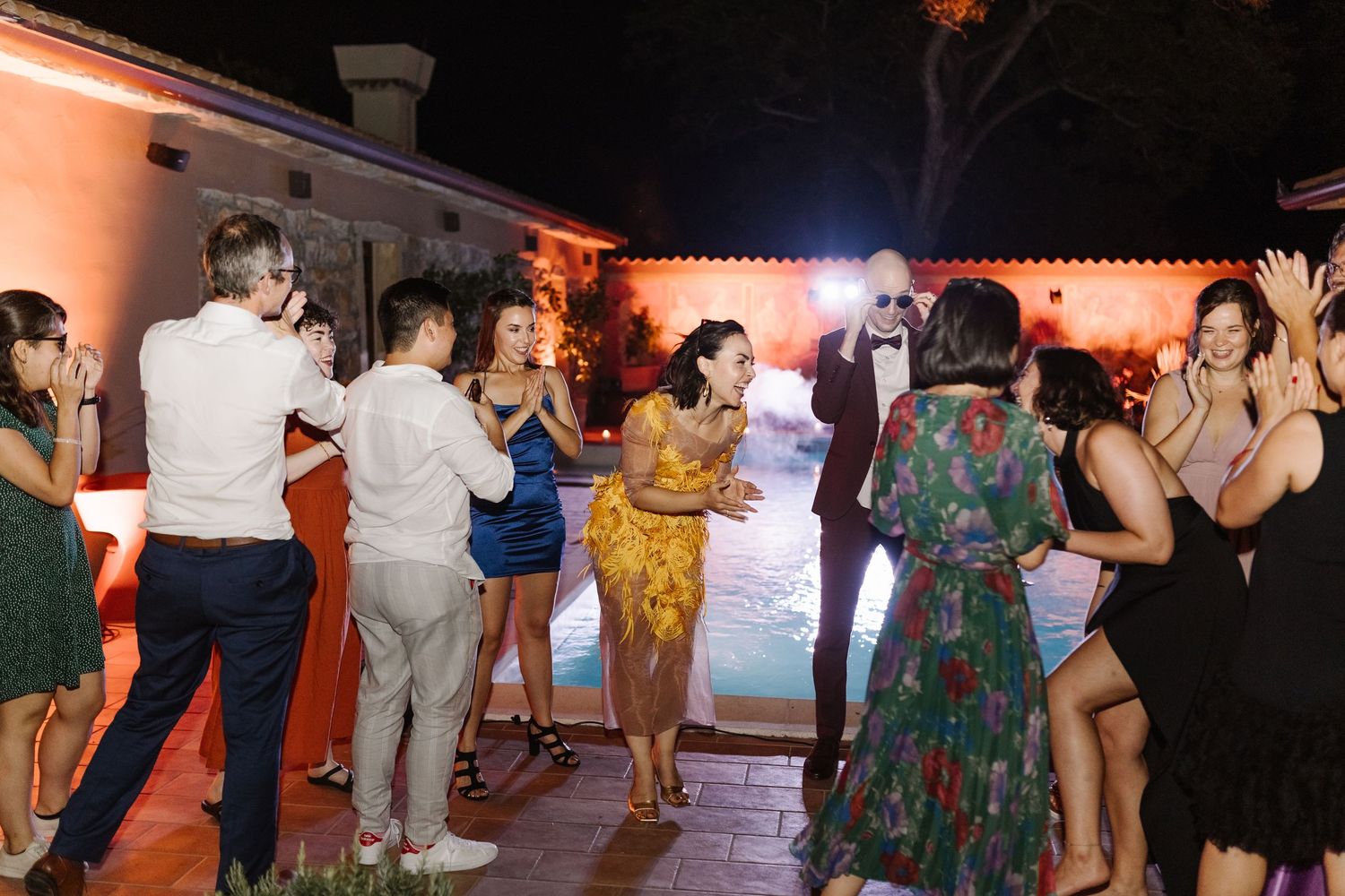 People dancing together at a lively reception party with orange ambient lighting in the background.