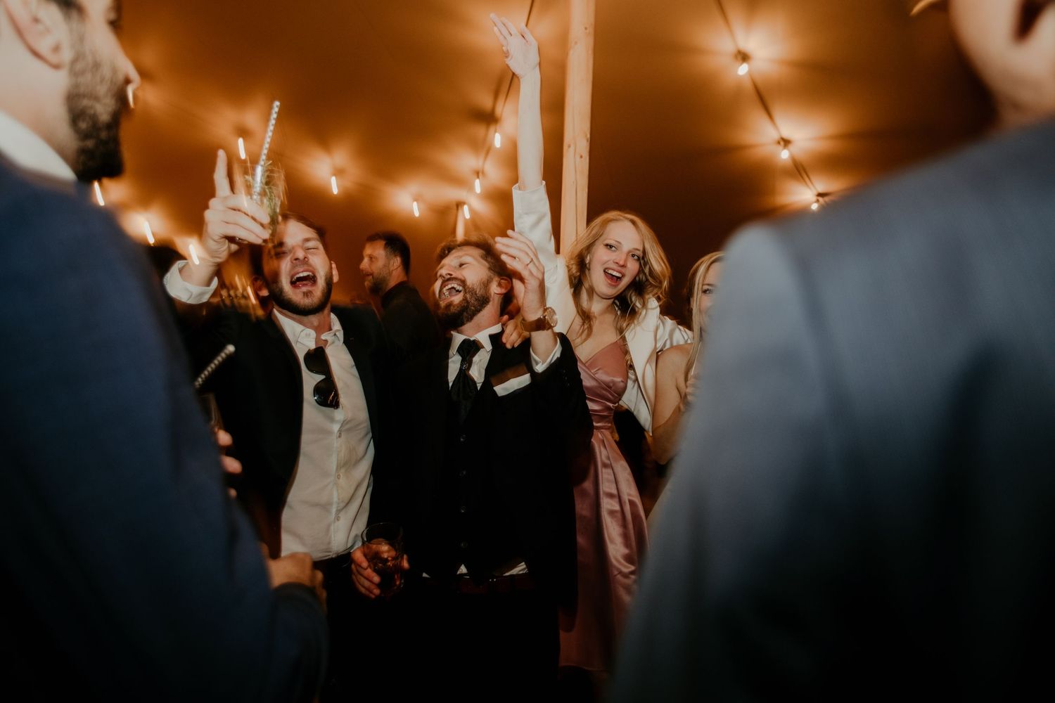 Wedding reception guests dancing and celebrating under warm amber lighting at an evening party.