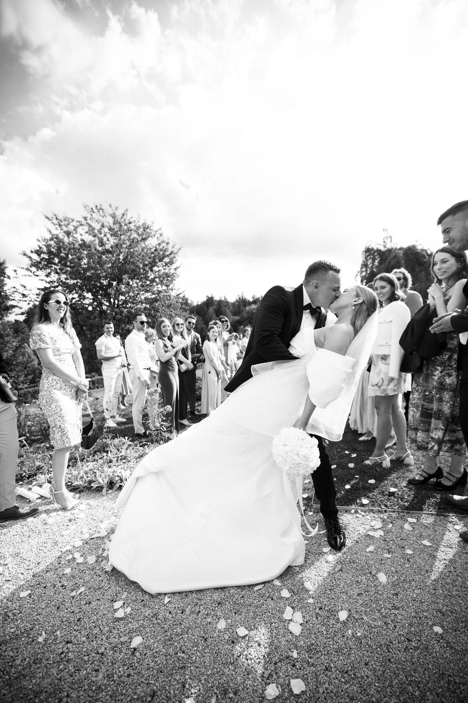 Black and white sequence of wedding guests throwing flower petals during an outdoor celebration.
