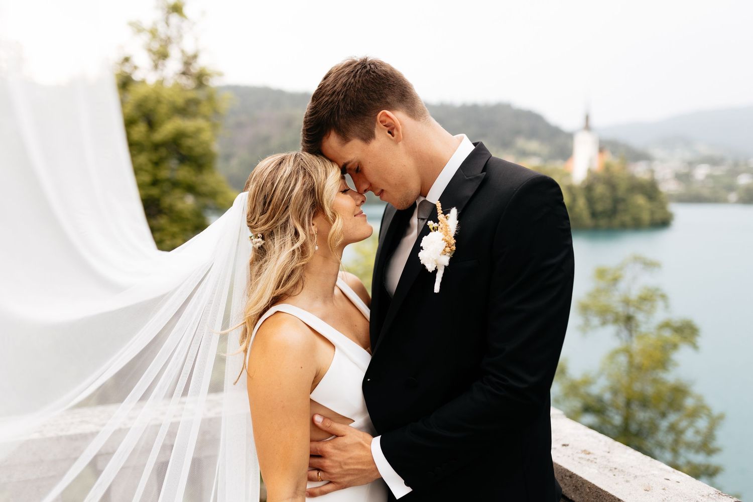 Romantic wedding portrait with flowing veil against a scenic lake and mountain backdrop.