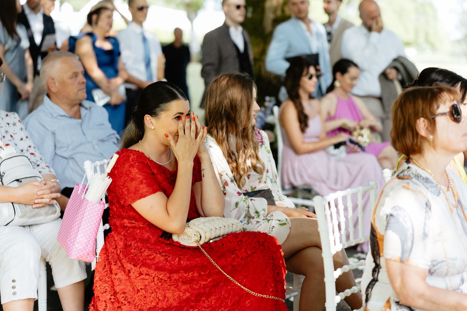 Wedding guests in colorful attire seated at outdoor reception tables with decorative pink and white decor.