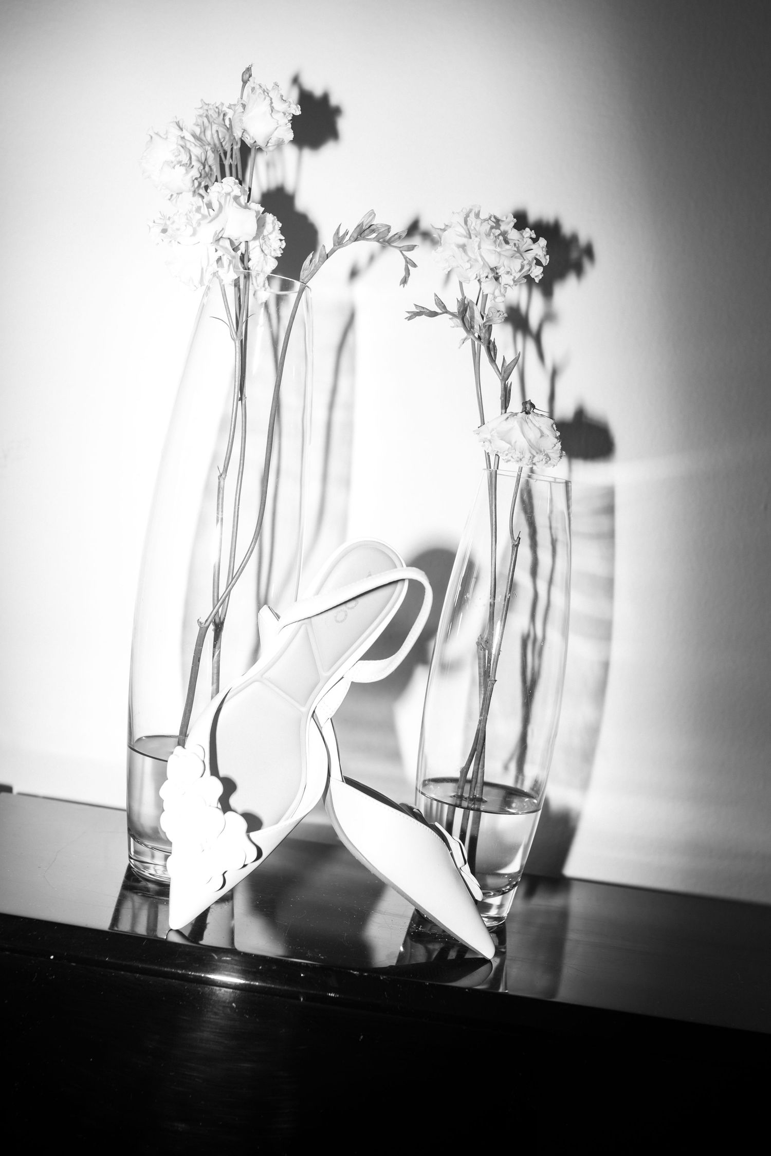 Artistic black and white still life composition of glass vases with flowers creating dramatic shadows and light patterns.