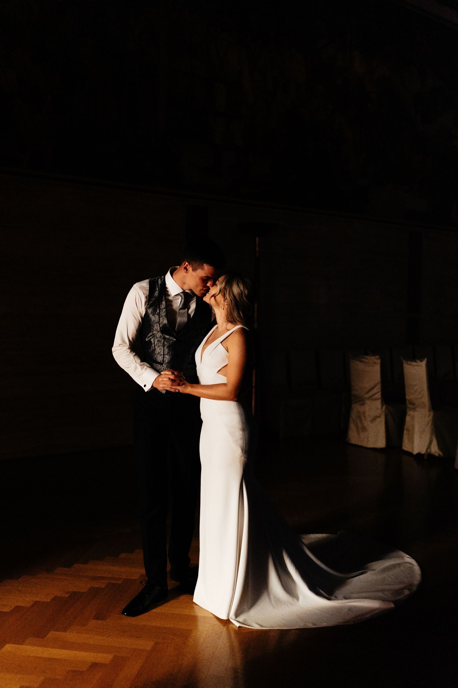 Dramatic spotlit first dance between newlyweds on a wooden dance floor.