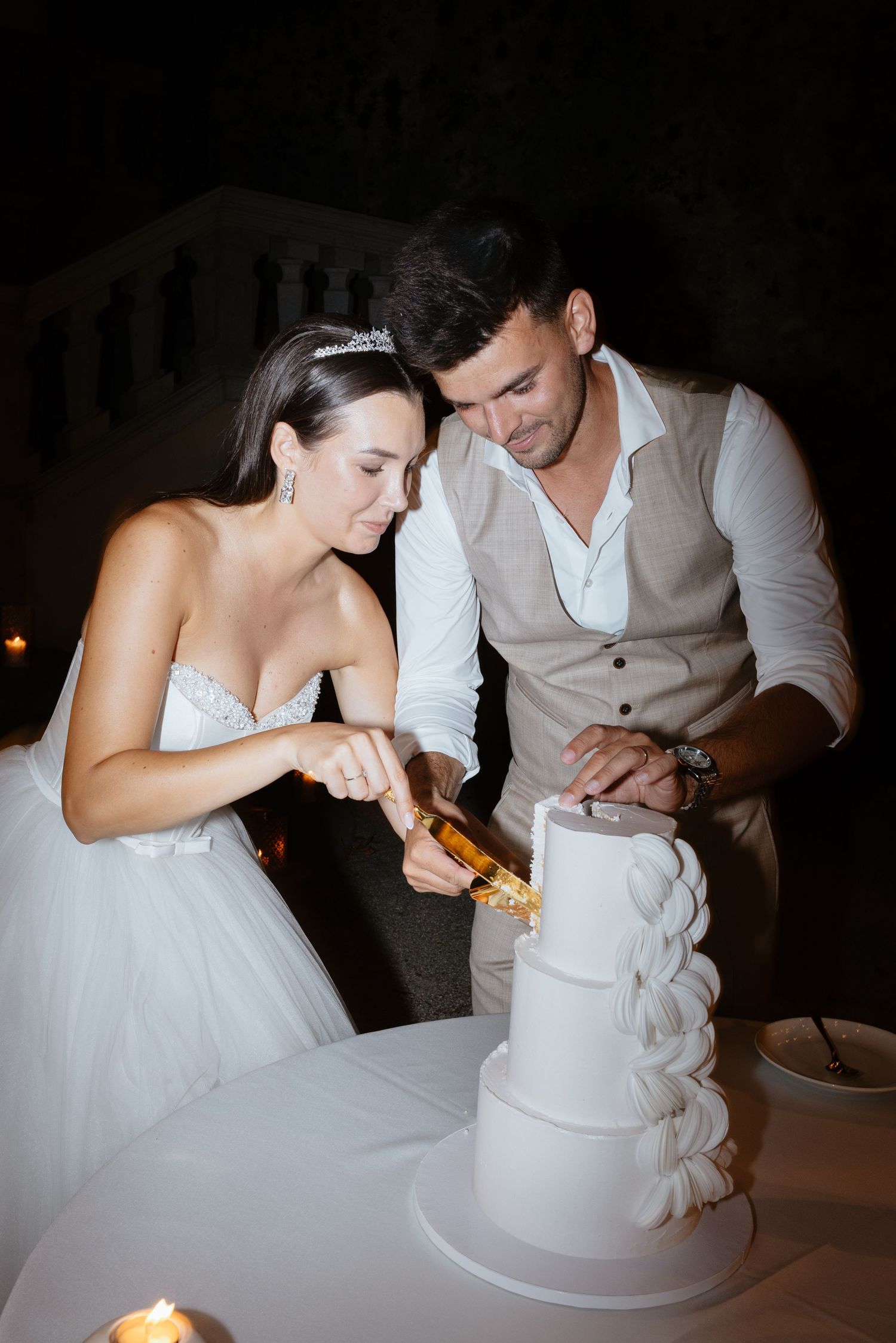 A couple shares an intimate moment while cutting their wedding cake by candlelight.