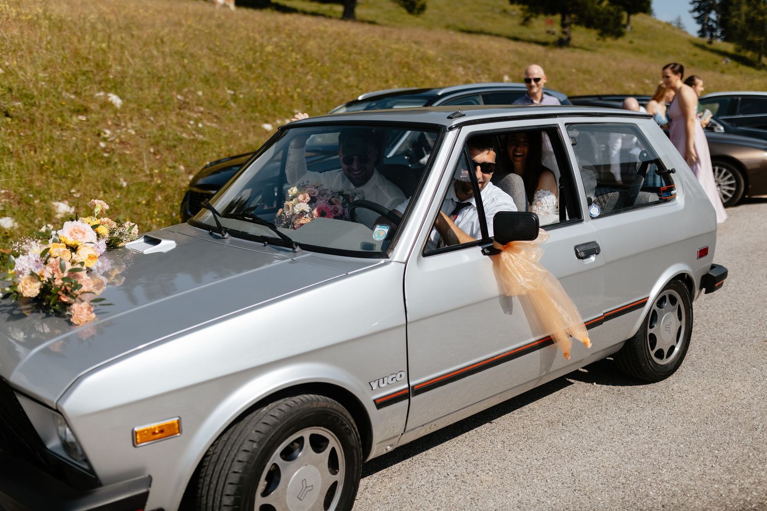 A silver convertible car decorated for a wedding sits parked on a sunny day.