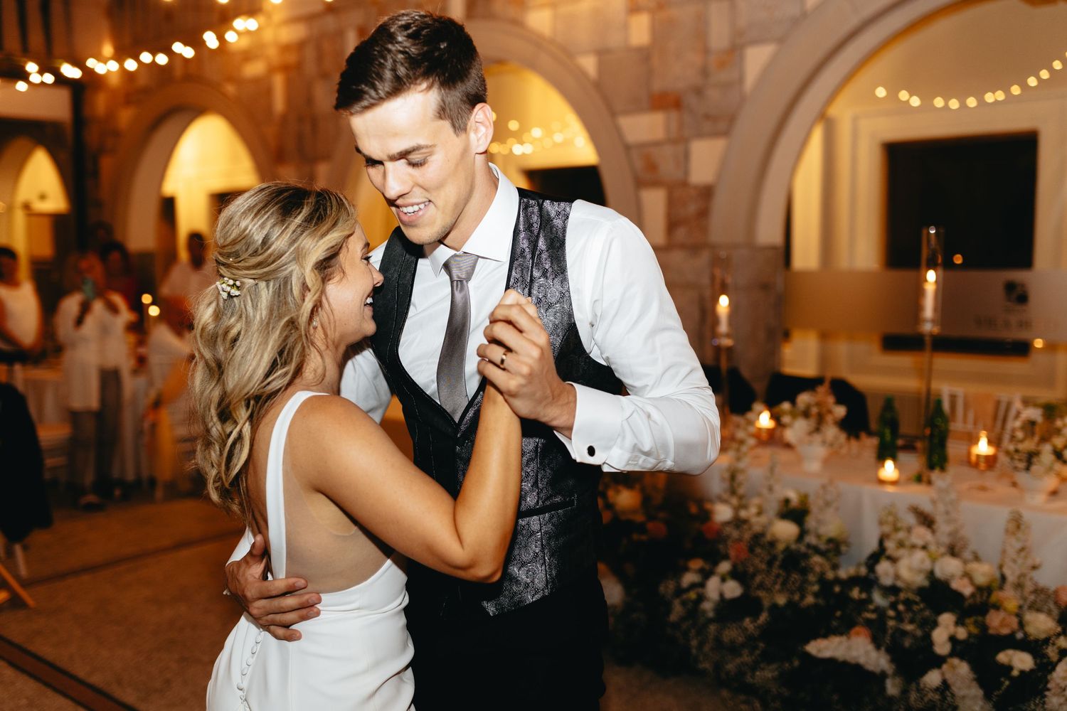Romantic evening reception scene with string lights and stone architecture in the background.