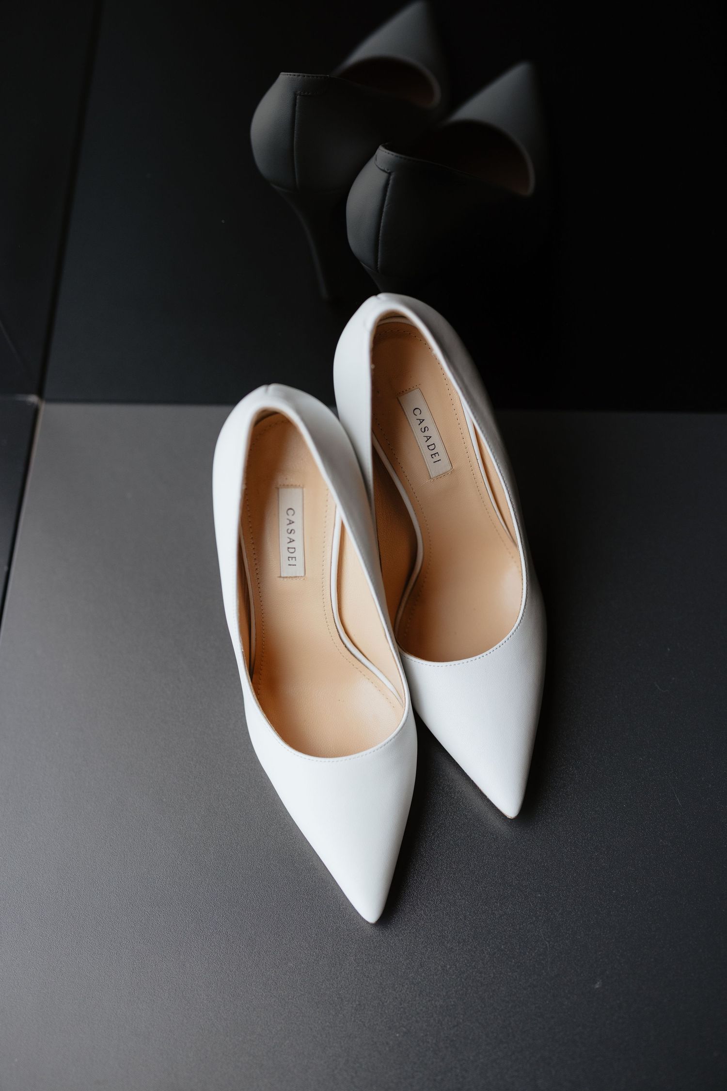 Elegant white pointed-toe bridal heels displayed against a dark background.