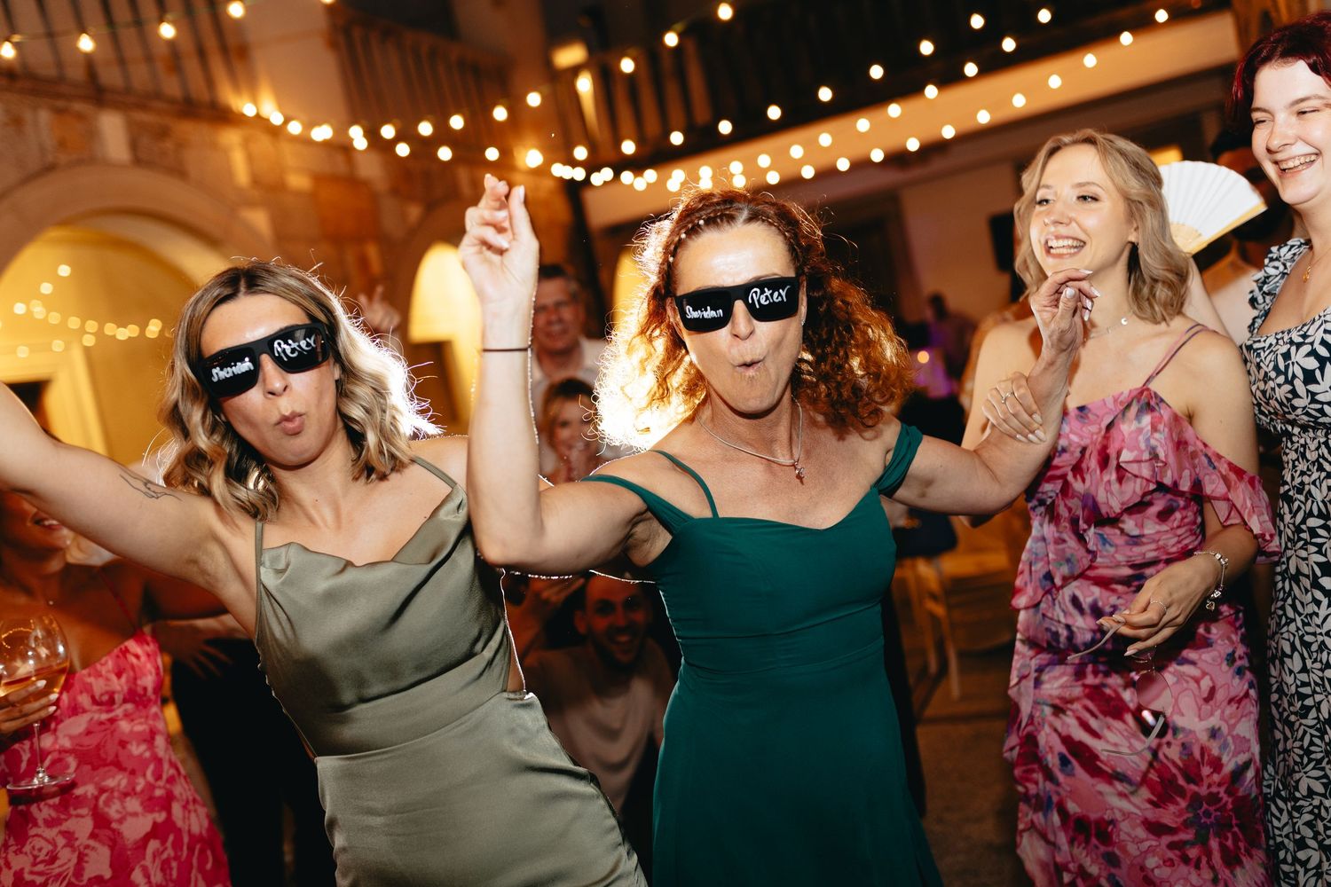 Wedding reception dance party with string lights and guests dancing.