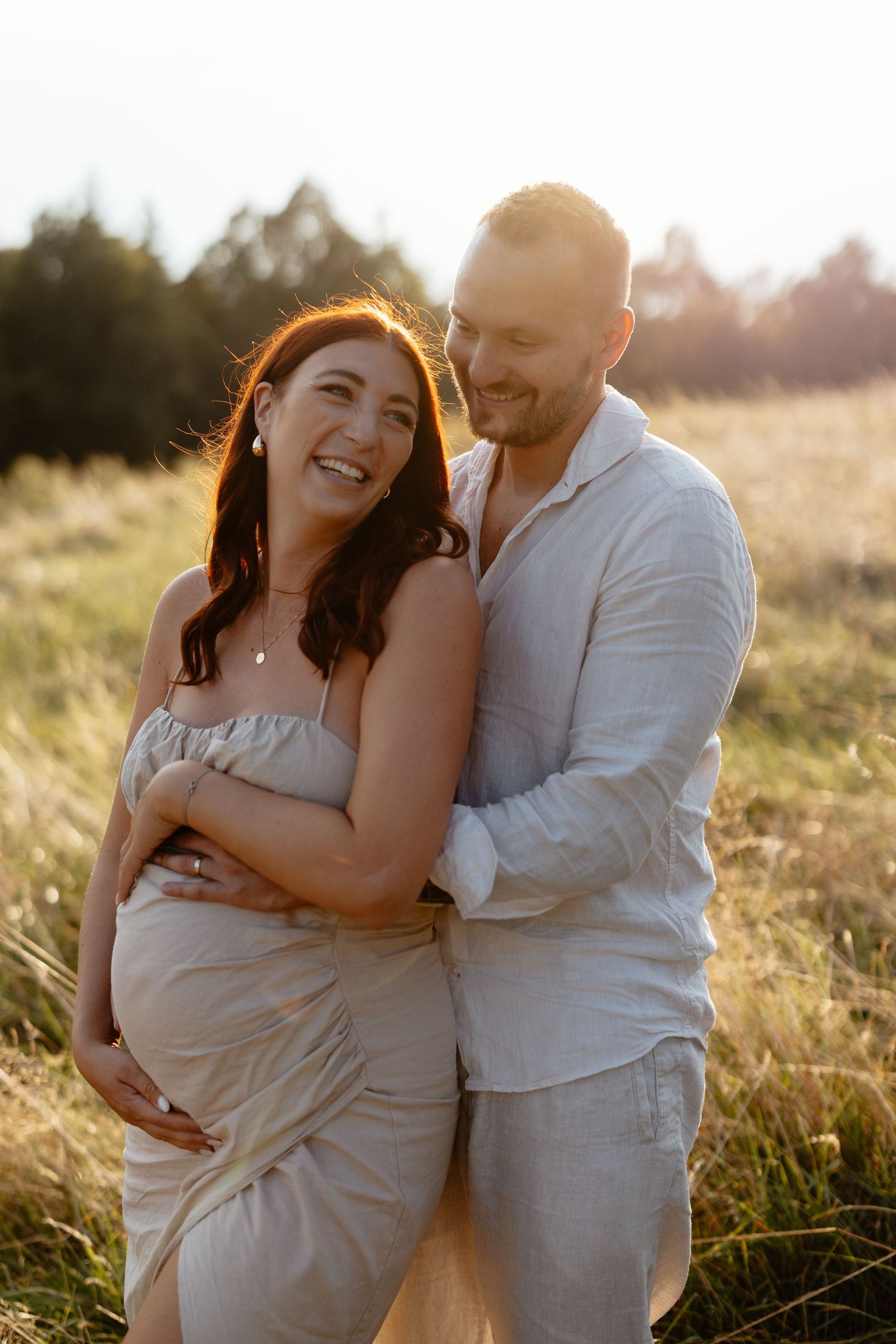 Maternity photos of couple embracing in golden sunset light.
