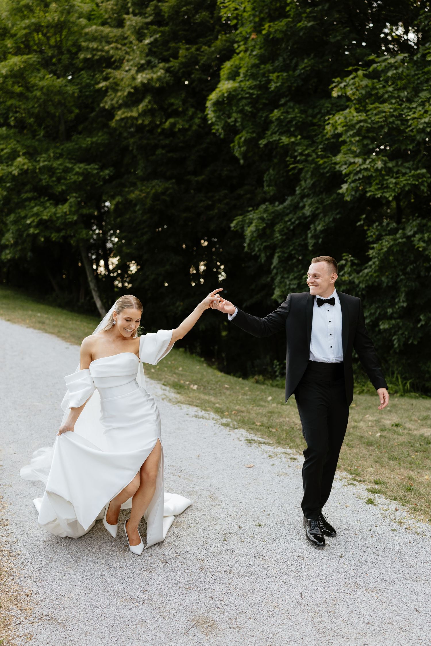 Wedding couple performing fun dance moves on a scenic gravel pathway.