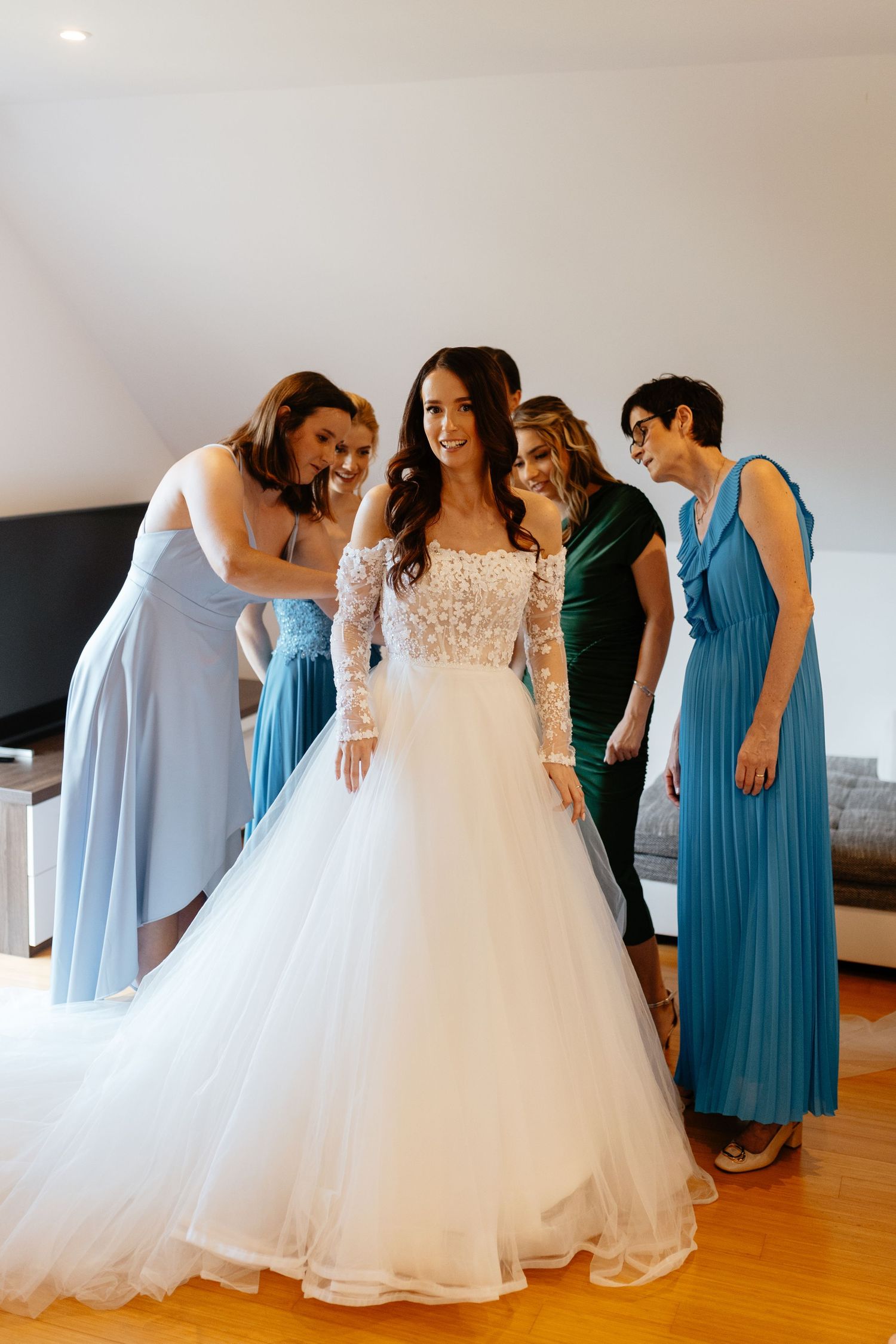 Bridesmaids in light blue and teal dresses gather around a bride wearing a stunning white ballgown during wedding preparations.