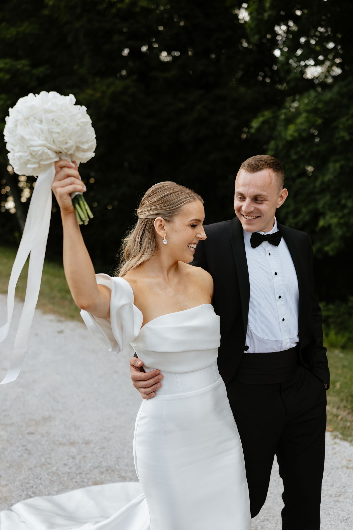 Elegant wedding couple sharing candid laughing moments on a gravel path.